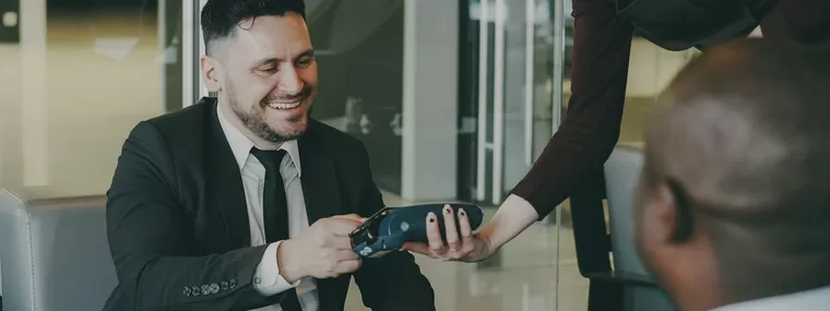 A server holds out a card terminal as a customer pays at a cafe table